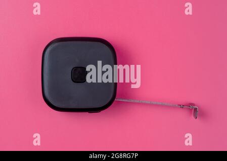 Measuring tape for construction work. Black roulette on a pink isolated background Stock Photo