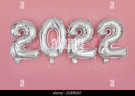 Silver foil balloons numeral 2022 and confetti on pink background Happy New year 2022 celebration Flat lay Stock Photo