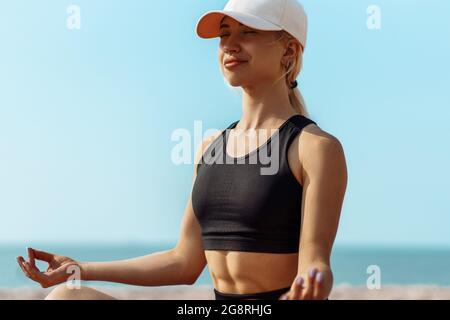 Sporty young woman doing yoga on the seashore, woman practicing yoga and meditation in lotus position on the beach, Beautiful woman relaxing on the se Stock Photo