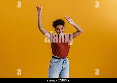 Happy casually dressed young african woman standing over yellow wall background, dancing Stock Photo