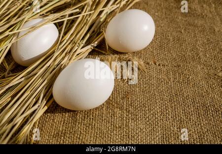 Three eggs on burlap partially in straw. The concept of celebrating the Christian holiday of Easter. Organic farm products. Stock Photo
