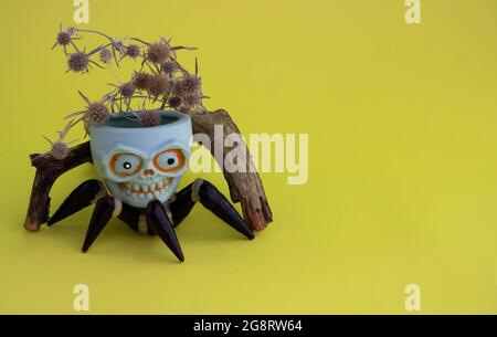 There is a snag on a yellow background, and a toy skull with spider legs. The concept of Halloween. Place for your text. Stock Photo