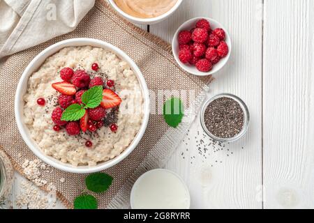 Oatmeal porridge with fresh berries, chia seeds and mint on a light background. Top view, copy space. Stock Photo