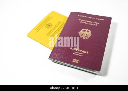 German Passport and yellow International Certificate of Vaccination book isolated on a white background, requirement to travel is a record for SARS-Co Stock Photo