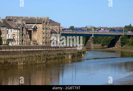 View down River Lune in Lancaster past St George's Quay to Carlisle Bridge with container train on the West Coast Main Line railway, 17th July 2021. Stock Photo