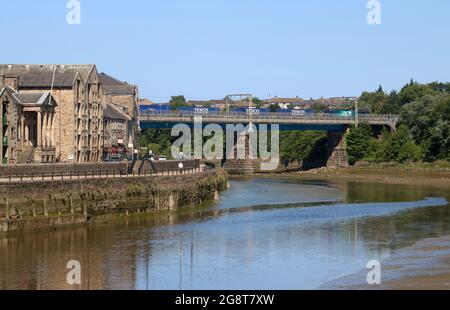 View down River Lune in Lancaster past St George's Quay to Carlisle Bridge with container train on the West Coast Main Line railway, 17th July 2021. Stock Photo