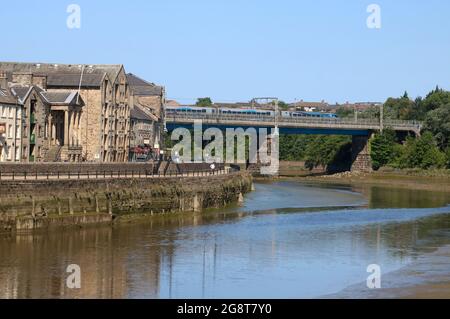 View down River Lune in Lancaster past St George's Quay to Carlisle Bridge with electric train on the West Coast Main Line railway, 17th July 2021. Stock Photo