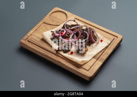 shashlik or grilled meat with onion on pita on wooden board on grey background Stock Photo