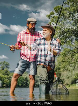 Grandfather and boy fishing together. Happy father and son fishing in river holding fishing rods. Brown trout fish. Father and son fishing. Stock Photo