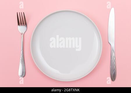 Empty White Ceramic Plate with Fork and Knife on Pink Background - Top View, Flat Lay Stock Photo