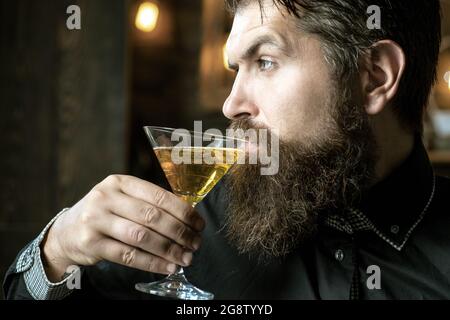 Handsome pensive man is holding a glass of martini. Handsome man drinking alcohol while sitting at the bar. Stock Photo