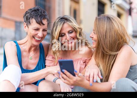 Three cheerful mature friends together using cell phone and laughing Stock Photo