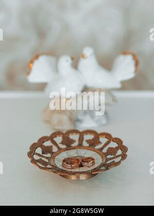 Two gold wedding bands symbolic of love and romance on a textured glitter plate with statuette in the form of white doves Stock Photo