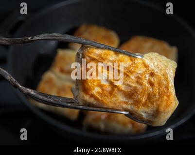 Close-up of freshly fried stuffed cabbage roll covered by delicate crust in metal kitchen tongs. Process of cooking homemade cabbage rolls. Unfocused Stock Photo