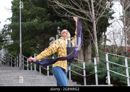 Young non binary person dancing and listening music in the street. Make up androgynous person. Stock Photo