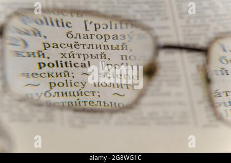 Reading glasses and an open book in close-up. Old Russian-English Dictionary. Selective Focus on the word POLITICAL. Stock Photo