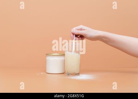 Womans hand mixes collagen powder or protein in a glass of water. Hydrolyzed collagen on a beige background. Natural healthy supplement. Copy space Stock Photo