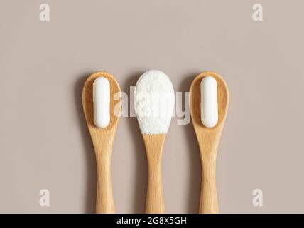 Collagen on a beige background. Collagen protein powder and pills in wooden spoons. Natural supplement. Top view, flat lay. Stock Photo