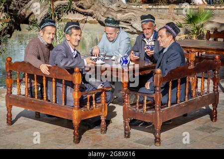 Group of Uzbek men wearing traditional hats drink tea in Bukhara, Uzbekistan Stock Photo