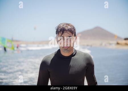 Portrait of a good looking Indian man, surfer at the beach looking at the camera, extreme sports and leisure activity - focus on face Stock Photo