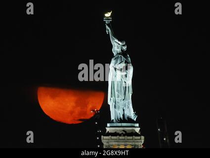New York, United States. 23rd July, 2021. A full Buck Moon, partially obstructed by clouds, sets behind the Statue of Liberty in New York City on Friday, July 23, 2021. Photo by John Angelillo/UPI Credit: UPI/Alamy Live News Stock Photo