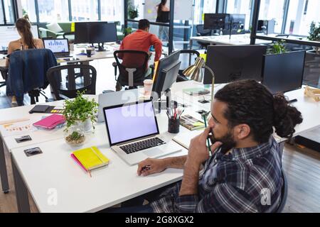 Mixed race male creative worker sitting at desk using laptop Stock Photo