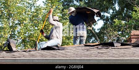 Construction workers removing and replacing roof shingles on a residential house Stock Photo