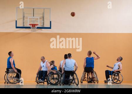 Disabled War veterans mixed race opposing basketball teams in wheelchairs photographed in action while playing an important match in a modern hall.  Stock Photo