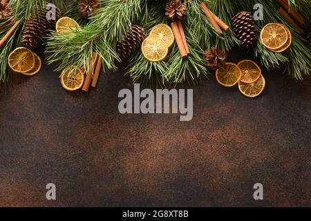 Christmas border with orange slice, aroma cinnamon, fir tree and cones on brown background. New Year. Top view. Xmas holiday greeting card. Copy space Stock Photo