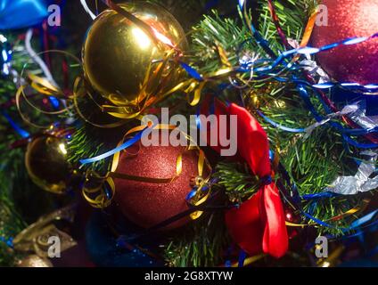 Red New Year's ball with glitters and ribbons on the decorated Christmas tree, close-up. Stock Photo