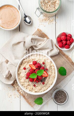 Oatmeal porridge with fresh raspberries, strawberries and red currants on a white background. Top view, close-up. Stock Photo