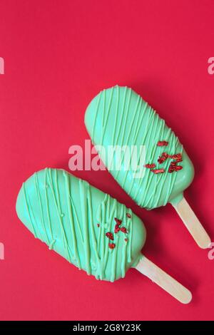 cake - popsicle in green glaze on a red background. space for text. Ice cream sweet eskimo with chocolate icing.  Chocolate covered ice cream on stick Stock Photo