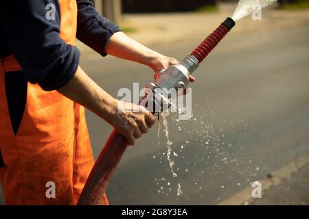 Water hose. The flow of water from the pipe. A man holds a fire hose. Stock Photo