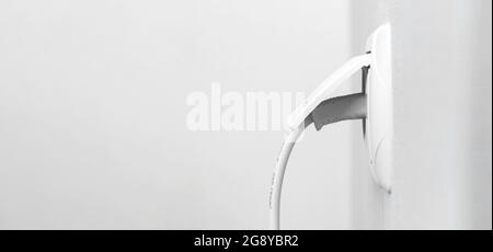 Cable plugged in a white electric outlet on white wall in modern interior, banner design with copy space Stock Photo