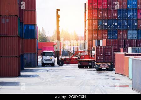 Forklift truck lifting cargo container in shipping yard or dock yard against sunrise sky with cargo container stack in background for transportation i Stock Photo