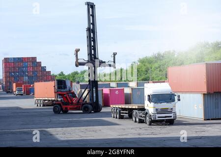 Forklift truck lifting cargo container in shipping yard or dock yard against sunrise sky with cargo container stack in background for transportation i Stock Photo