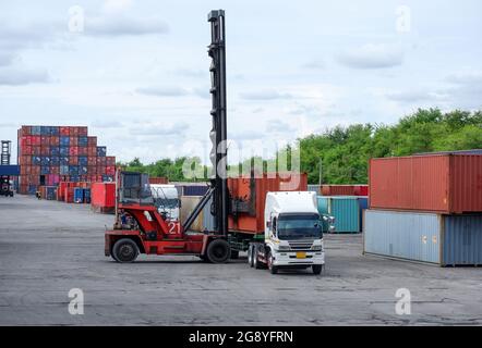 Forklift truck lifting cargo container in shipping yard or dock yard against sunrise sky with cargo container stack in background for transportation i Stock Photo