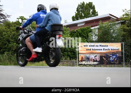 Leer, Germany. 23rd July, 2021. A motorcycle rides past a house with a banner on the fence that reads '. we are at home and can hear you'. Hundreds of motorcyclists are expected in the town in East Frisia on Saturday to make a seriously ill six-year-old boy happy with a parade. The police are even preparing for several thousand bikers. Credit: Lars Klemmer/dpa /dpa/Alamy Live News Stock Photo