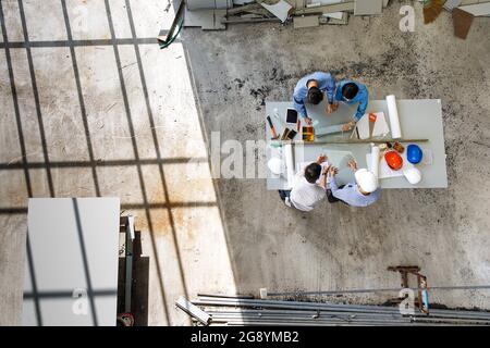 Four engineers in team making a discussion at construction site with several color helmets, taken from  bird eye views or top view Stock Photo