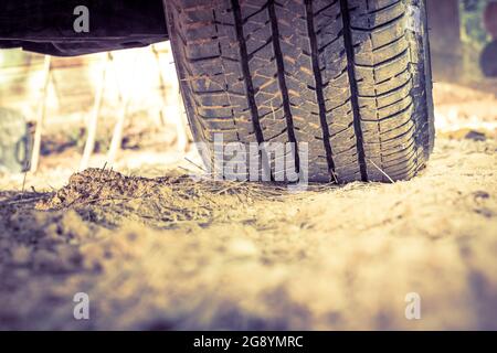 Closeup car tire on the ground. Wheel tracks on dirt, shallow depth of field (DOF) tyre in focus. Vintage picture style Stock Photo