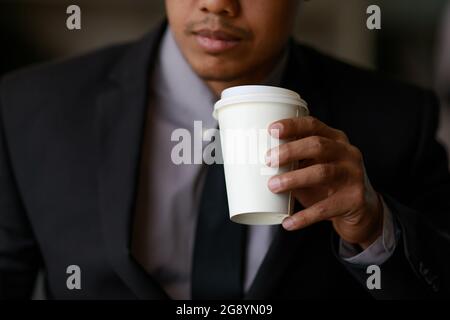Businessman in black suit holding white paper coffee cup Stock Photo