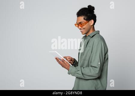 smiling and trendy african american man using digital tablet isolated on grey Stock Photo