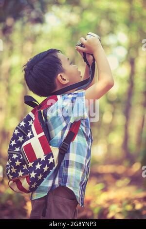 Asian boy taking photos by professional digital camera on blurred background. Photo in retro style. Smart child in nature. Outdoors portrait. Photo in Stock Photo