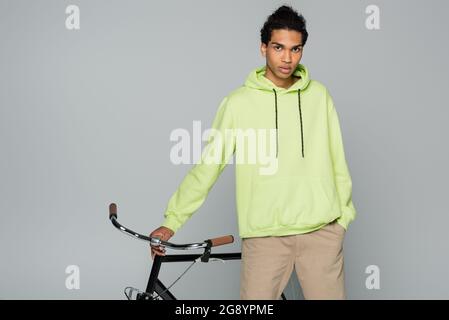 african american man in green hoodie looking at camera near bike on grey background Stock Photo