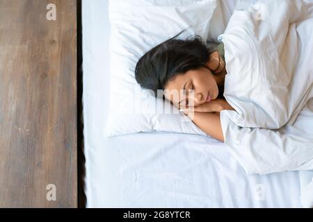 Top view of a sleeping asian woman. She lies under the blanket and hugs the pillow. Healthy sleep concept. Stock Photo