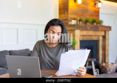 Asian woman works with documents in front of a laptop monitor. She checks the tax records before submitting the report. Modern technology in everyday Stock Photo