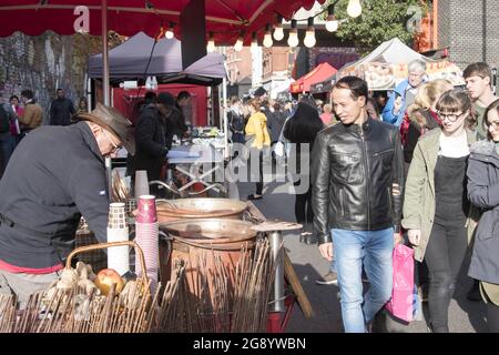 Millennial generation visitors look on as a man cooks street food at the Brick Lane Market, a major shopping district and outdoor market for secondhand goods in Tower Hamlets, East London, United Kingdom, October 29, 2017. (Photo by Smith Collection/Gado/Sipa USA) Stock Photo