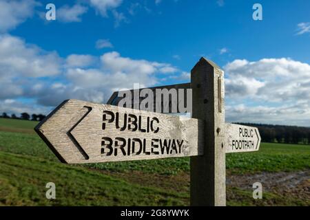 Wooden public bridleway sign in the countryside with blue sky and fields. Stock Photo