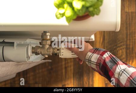 Close-up view of caucasian female's hand adjusting home radiator temperature by using thermostat, modern interior background Stock Photo