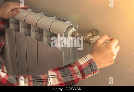 Close-up of woman hand on thermostatic valve of radiator heater in apartment Stock Photo